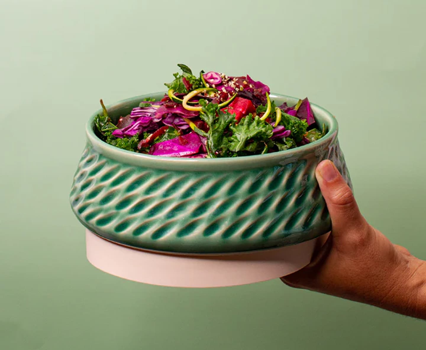 Hand holding a green fluted ceramic bowl filled with salad